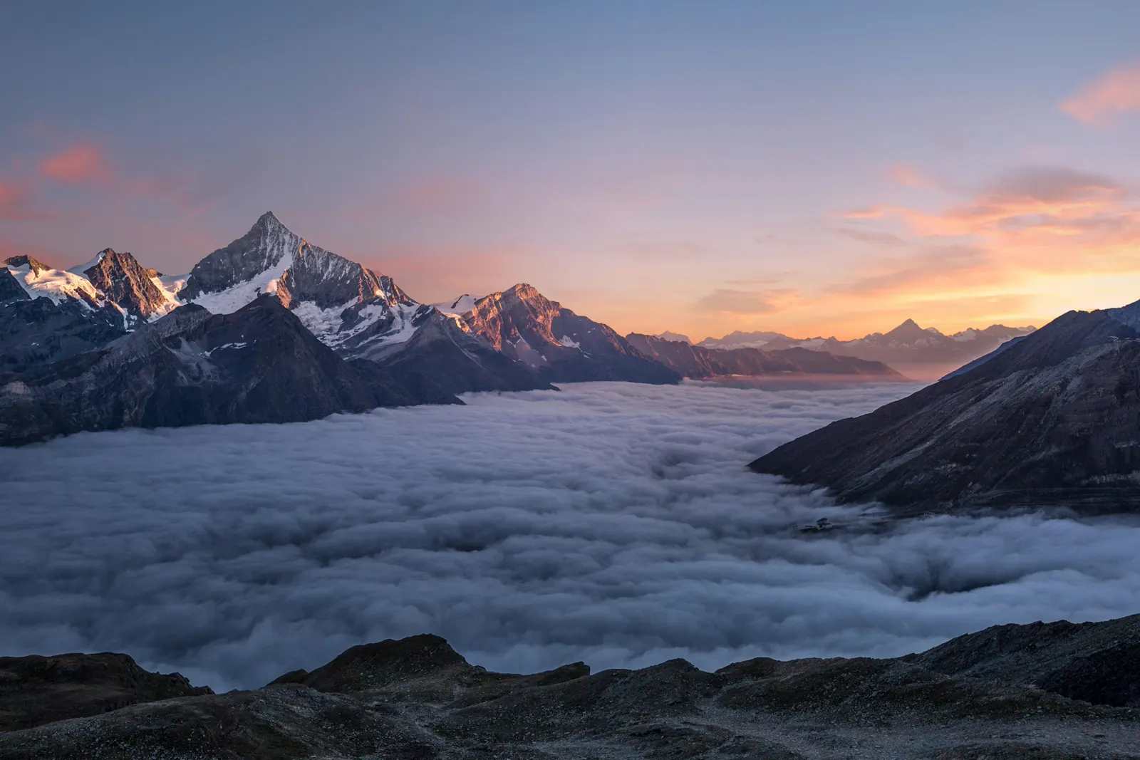 Snow-capped mountain peaks rising above a sea of clouds at sunset